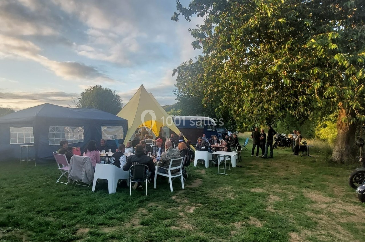 Groupe de personnes assises autour de tables en plein air sous des tentes, dans un jardin par temps ensoleillé.