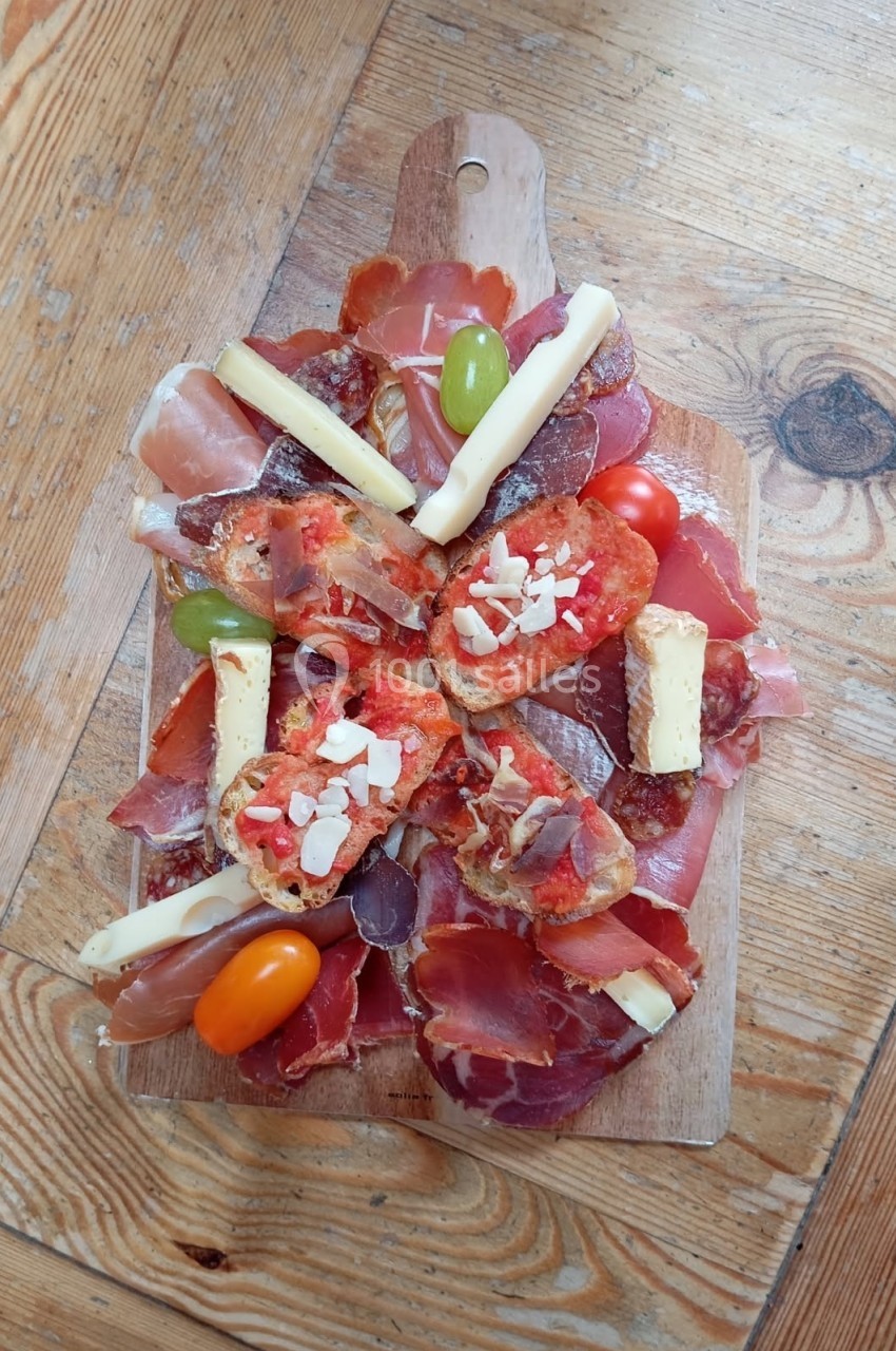 Planche en bois garnie de charcuteries, fromages, olives, tomates cerises et tranches de pain grillé.