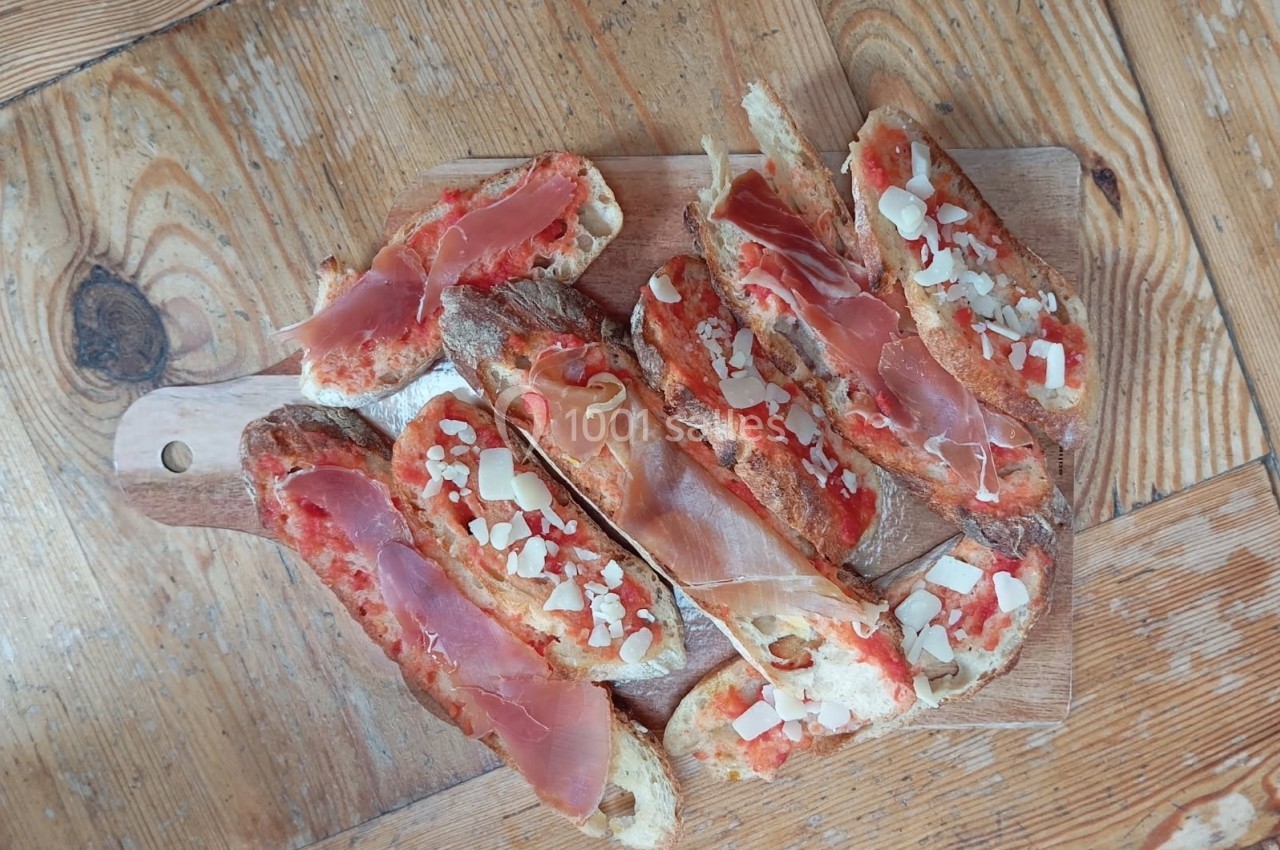 Tranches de pain garnies de jambon cru, tomate et copeaux de fromage sur une planche en bois.