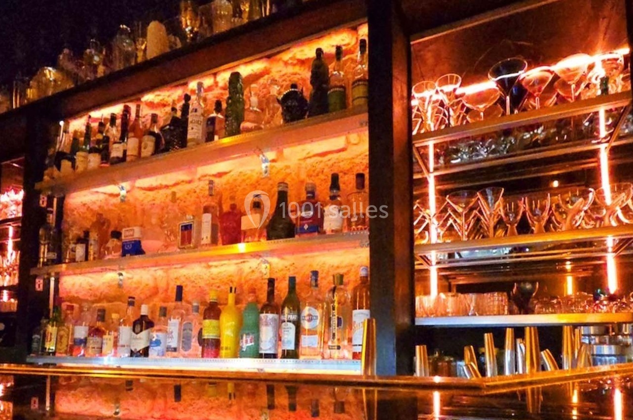 Étagères éclairées d'un bar avec bouteilles d'alcool et verres disposés sur un fond de mur en pierre.