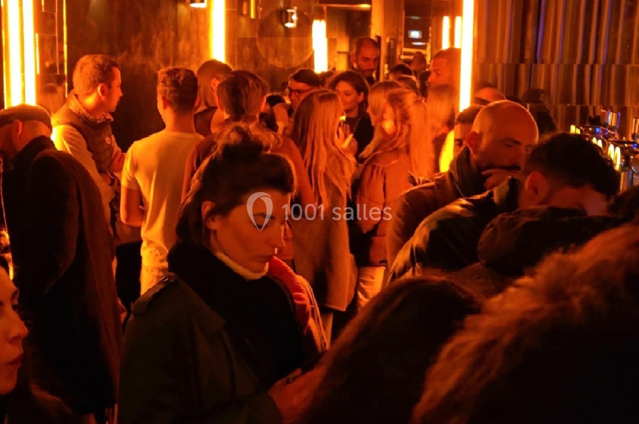 Groupe de personnes dans un bar à l'éclairage tamisé avec des tons chauds et une ambiance animée.