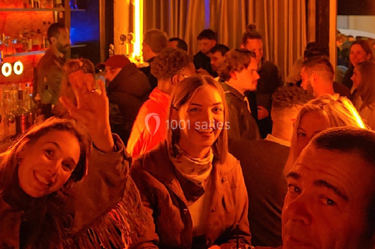 Groupe de personnes dans un bar animé avec éclairage chaleureux, discutant et profitant de l'ambiance conviviale.