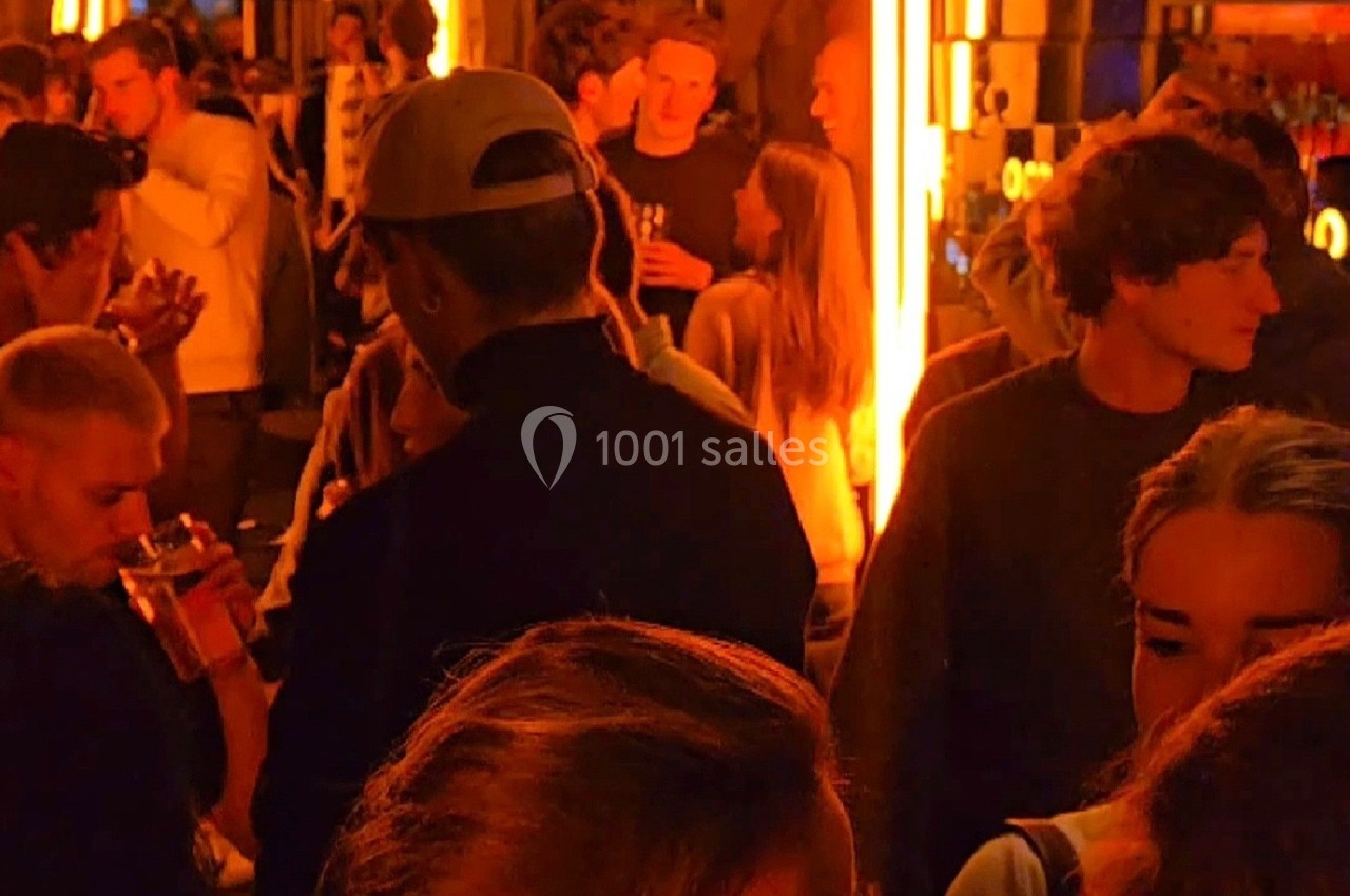 Groupe de personnes discutant et buvant dans un lieu animé avec un éclairage chaud et tamisé.