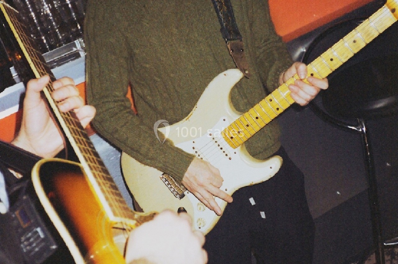 Deux musiciens jouent de la guitare électrique et acoustique dans un environnement intérieur.