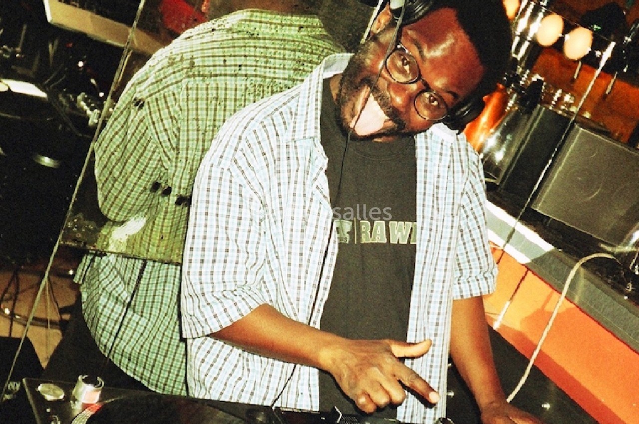 Un DJ souriant portant un casque audio mixe des disques vinyles sur une platine dans un environnement lumineux.