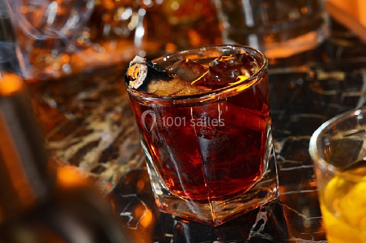 Verre de cocktail ambré avec glaçons et garniture, posé sur une table en marbre sombre.