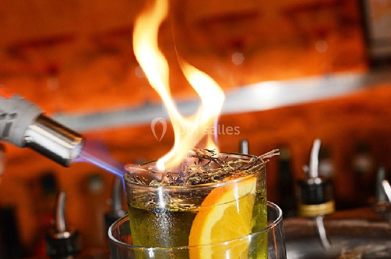 Cocktail enflammé avec une tranche d'orange, flambé à l'aide d'un chalumeau dans un bar.