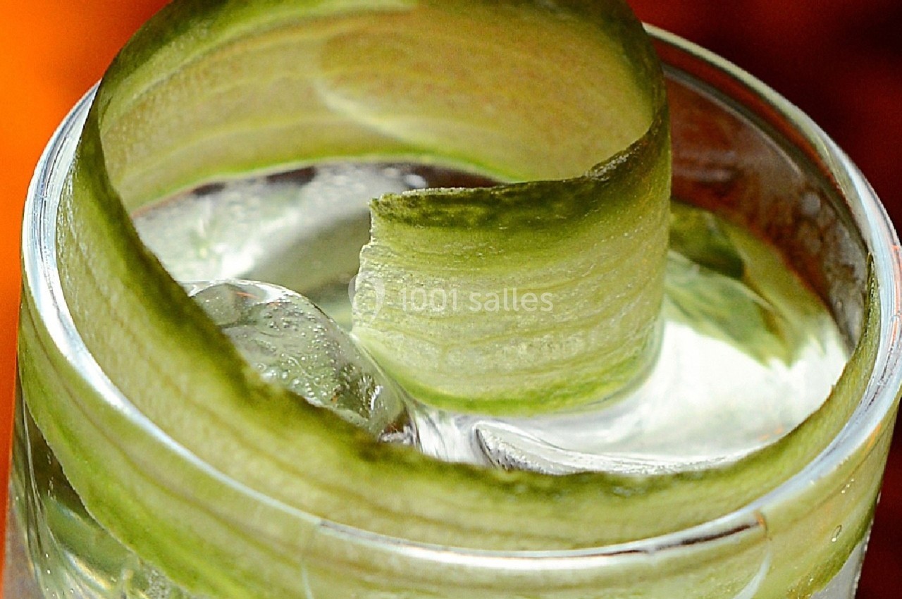 Tranche de concombre en spirale posée sur un verre rempli de glaçons et d'eau.
