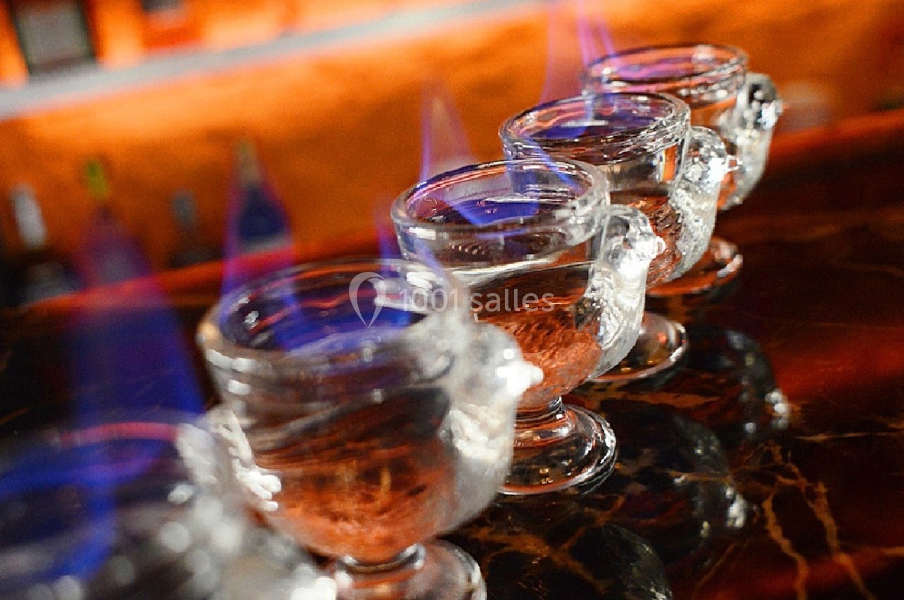 Quatre verres en verre transparent alignés sur un comptoir, contenant un liquide enflammé.