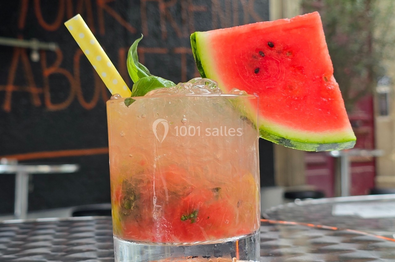 Verre de cocktail frais garni de pastèque, basilic et paille jaune, posé sur une table en extérieur.