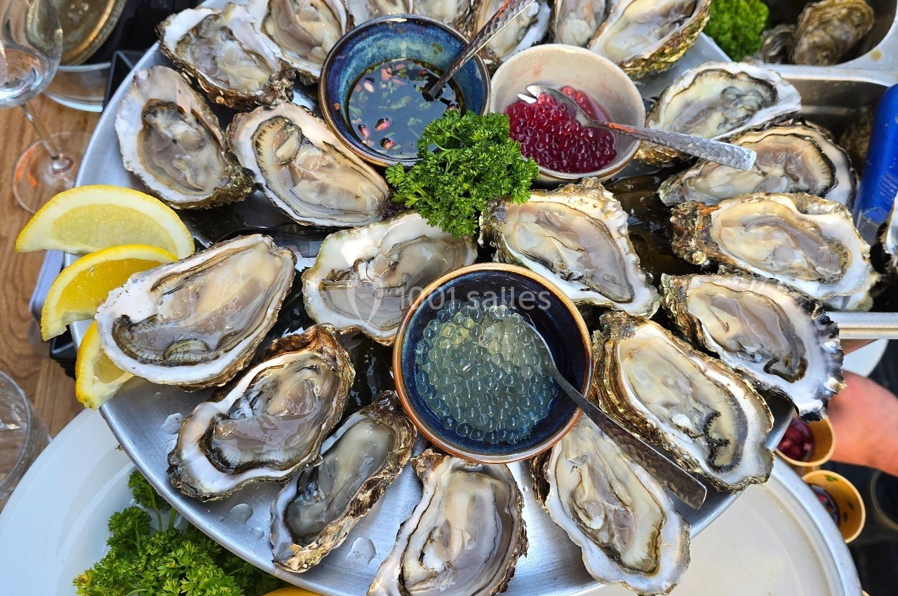 Plateau d'huîtres fraîches disposées autour de sauces, accompagné de quartiers de citron et de persil.