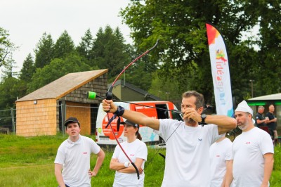 Un groupe de personnes en t-shirts verts participe à une activité de fléchettes géantes en plein air.