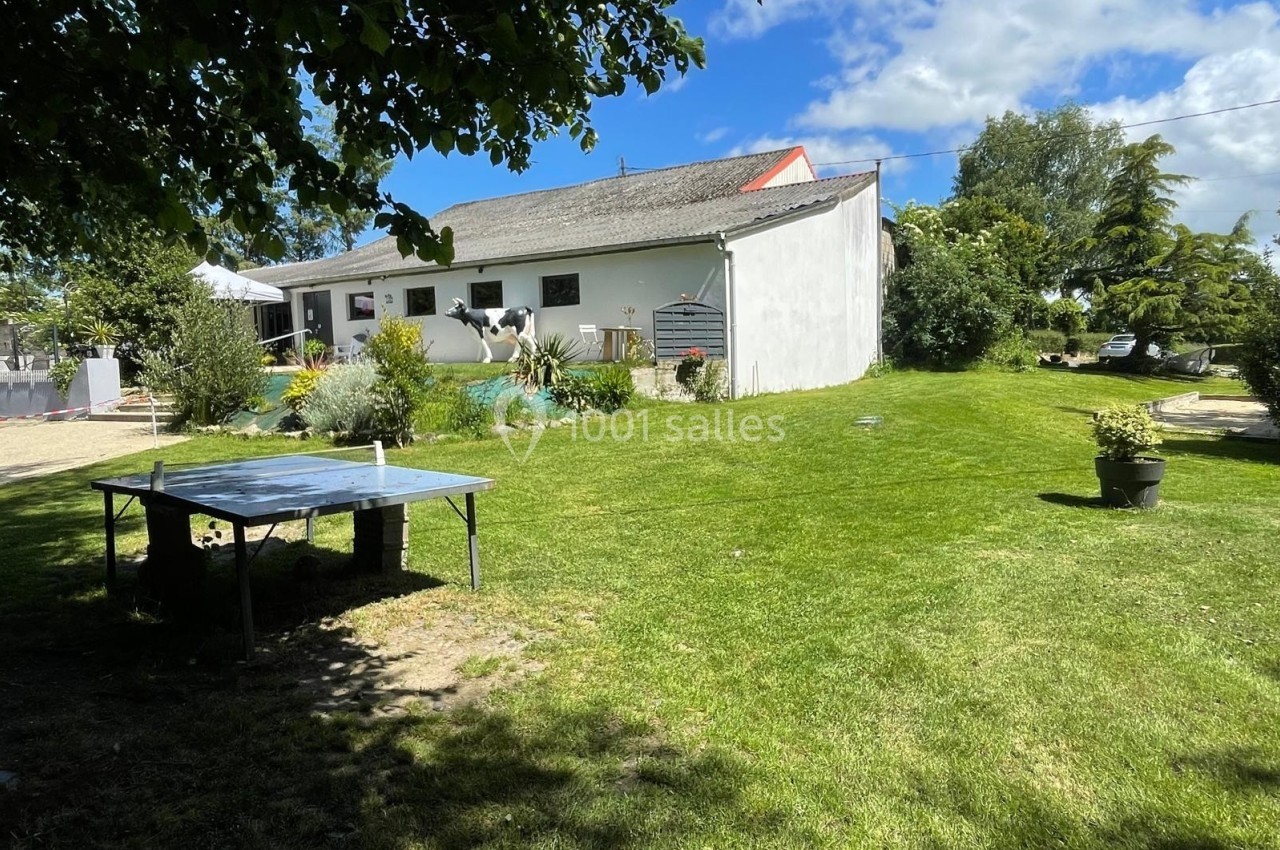 Jardin verdoyant avec pelouse, table de ping-pong, plantes en pot et maison blanche en arrière-plan sous un ciel bleu.