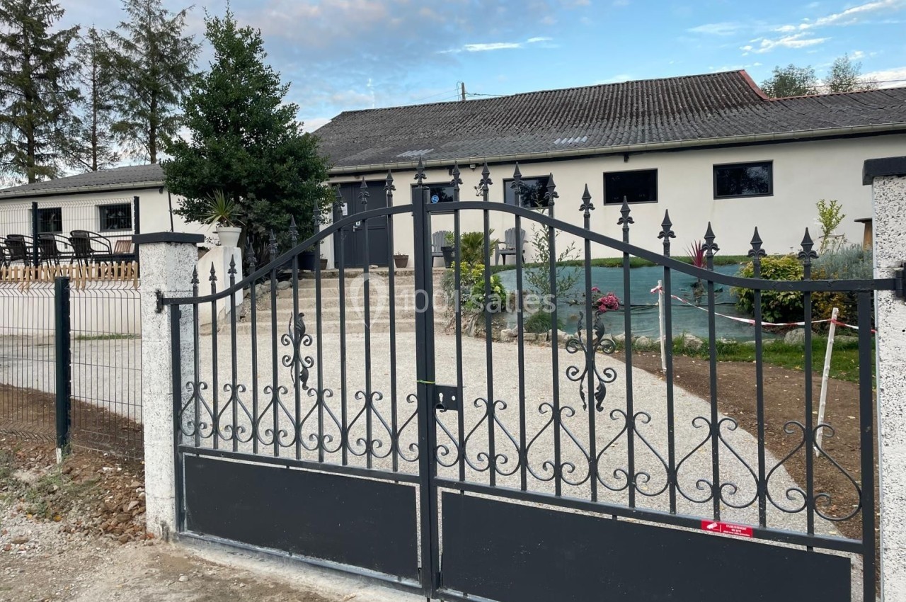 Portail en métal noir orné de motifs, donnant accès à une maison avec jardin et terrasse en arrière-plan.