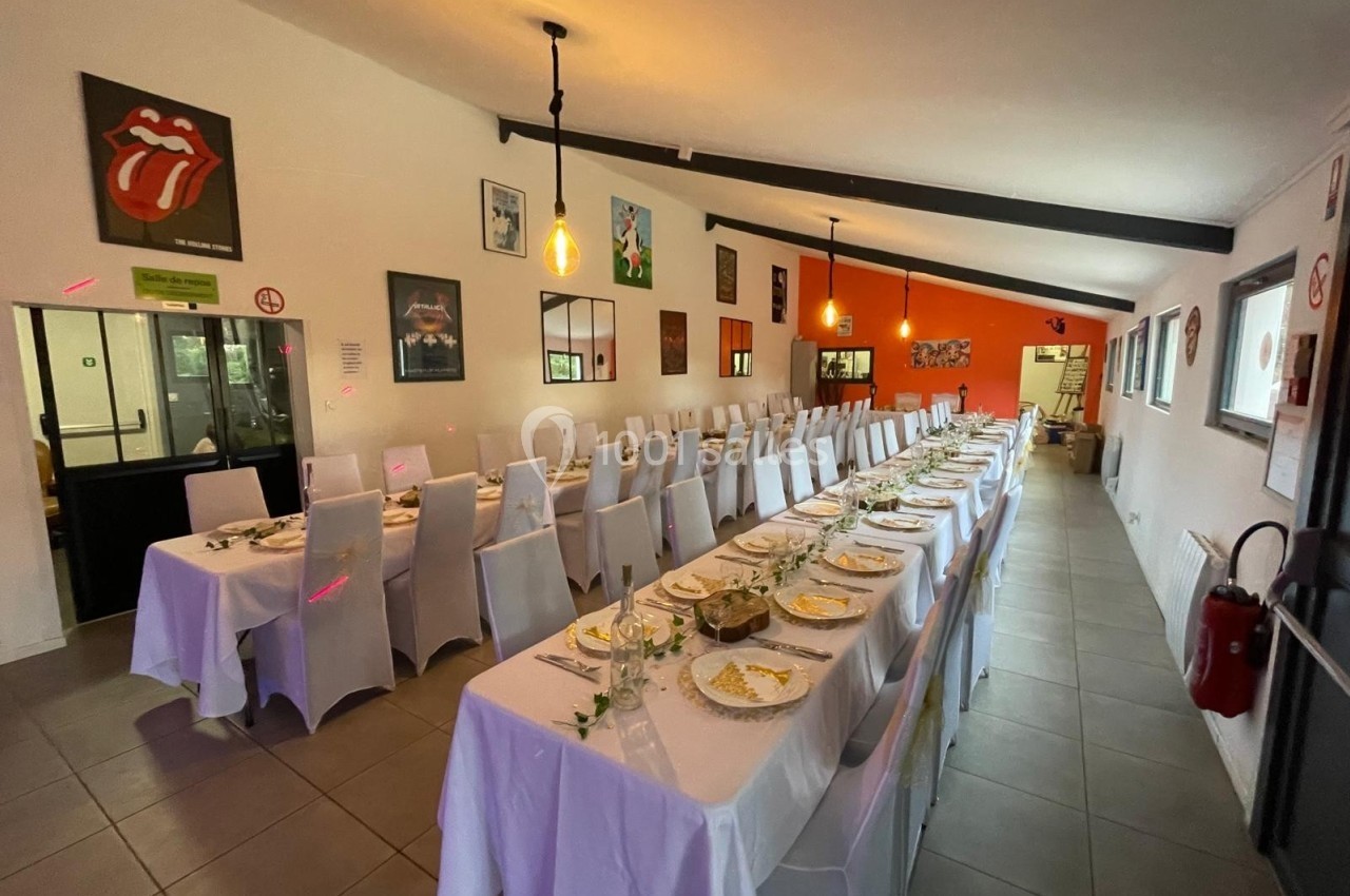 Salle de réception avec de longues tables dressées, nappes blanches et décorations murales colorées.