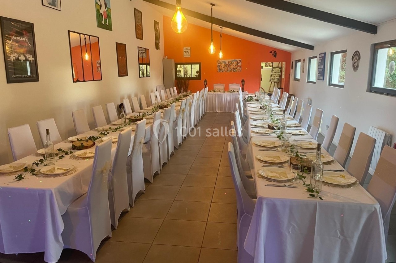 Salle décorée pour un repas avec deux longues tables dressées, nappes blanches et chaises alignées.