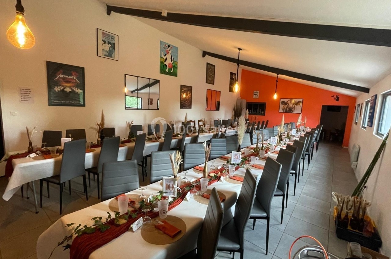Salle décorée pour un événement avec de longues tables dressées, chaises noires et murs ornés de cadres.