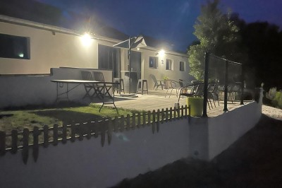 Maison moderne éclairée la nuit, entourée d'un jardin avec des arbustes et des fleurs.