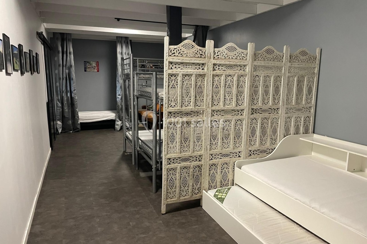 Un dortoir avec lits superposés, lit simple et cloison décorative en bois, dans un espace sobre et lumineux.