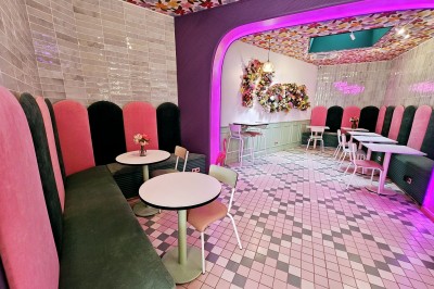 Salle de café colorée avec décoration florale murale, néons roses, mobilier pastel et ambiance lumineuse.