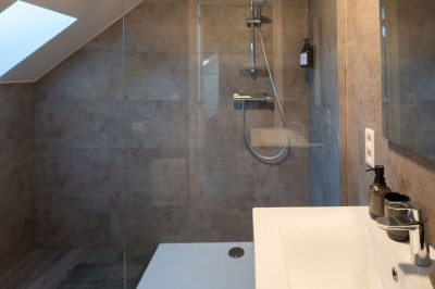 Salle de bain moderne avec douche à l'italienne, paroi en verre, lavabo blanc et éclairage intégré.