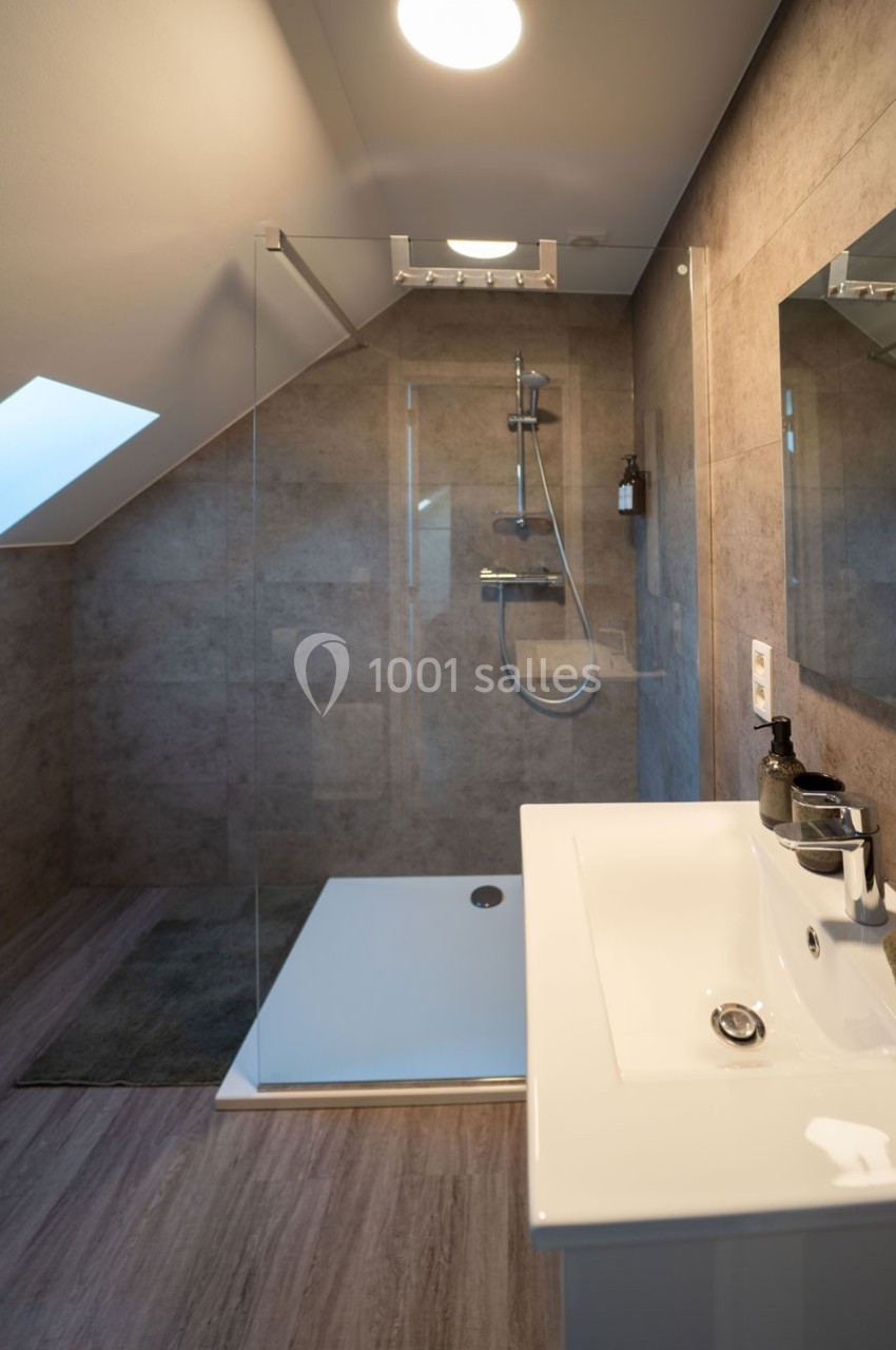 Salle de bain moderne avec douche à l'italienne, paroi en verre, lavabo blanc et éclairage intégré.