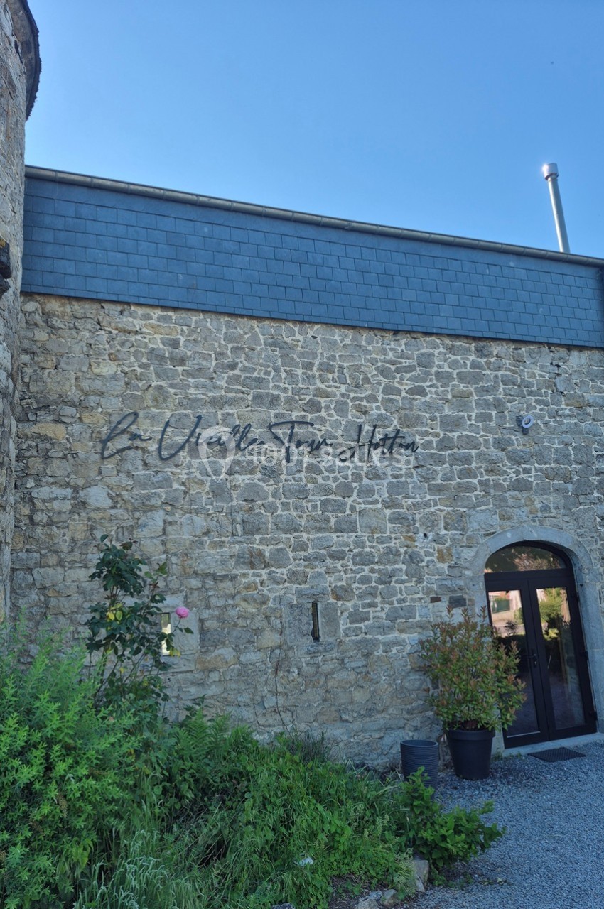 Façade en pierre d'un bâtiment avec une porte vitrée et des plantes en pot, sous un ciel dégagé.