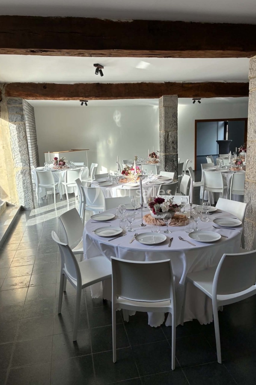 Salle lumineuse avec tables rondes dressées de nappes blanches, décorations florales et chaises blanches modernes.
