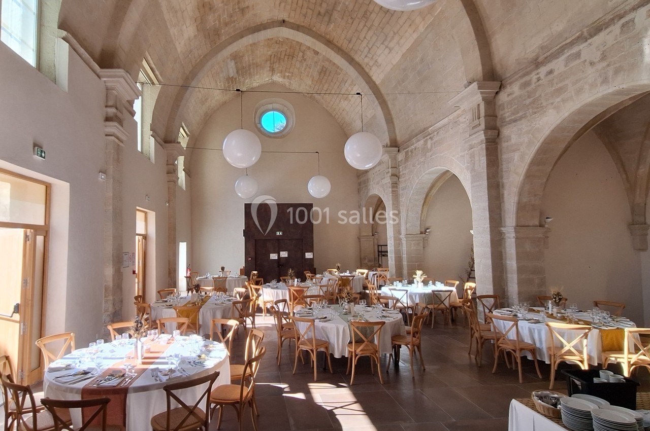 Salle voûtée lumineuse avec tables rondes dressées pour un événement, décorée de suspensions sphériques blanches.