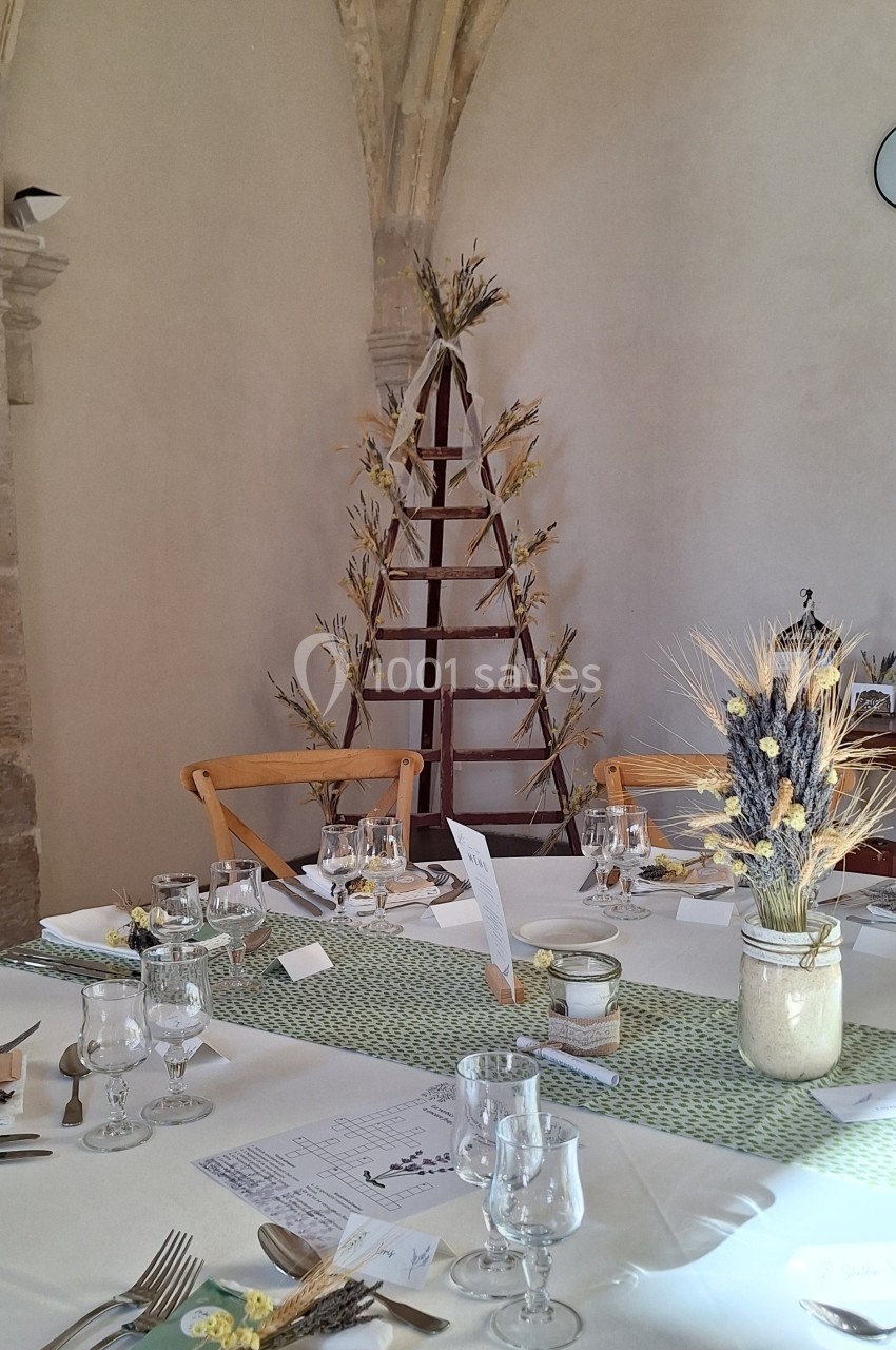Table décorée pour un repas, avec vaisselle élégante, centre de table floral et arrière-plan en pierre voûtée.