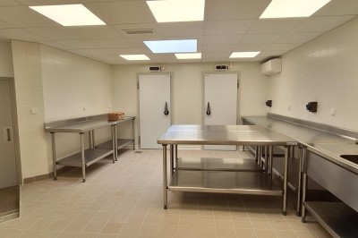 Cuisine professionnelle avec plans de travail en inox, évier, étagères et deux grandes portes de chambre froide.