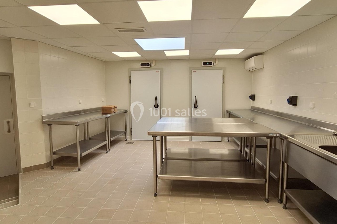 Cuisine professionnelle avec plans de travail en inox, évier, étagères et deux grandes portes de chambre froide.