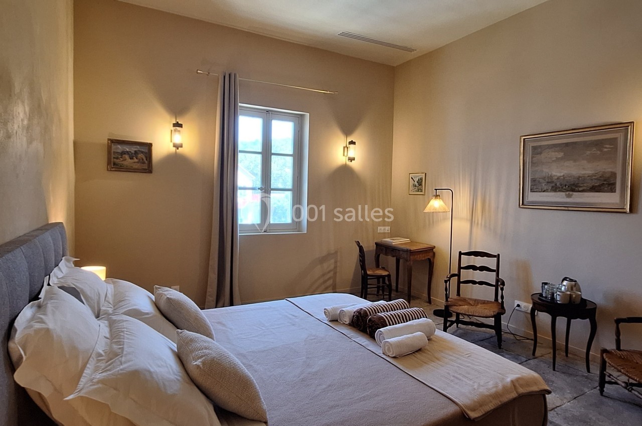 Chambre lumineuse avec lit double, bureau en bois, chaises anciennes et décoration murale dans un style chaleureux.