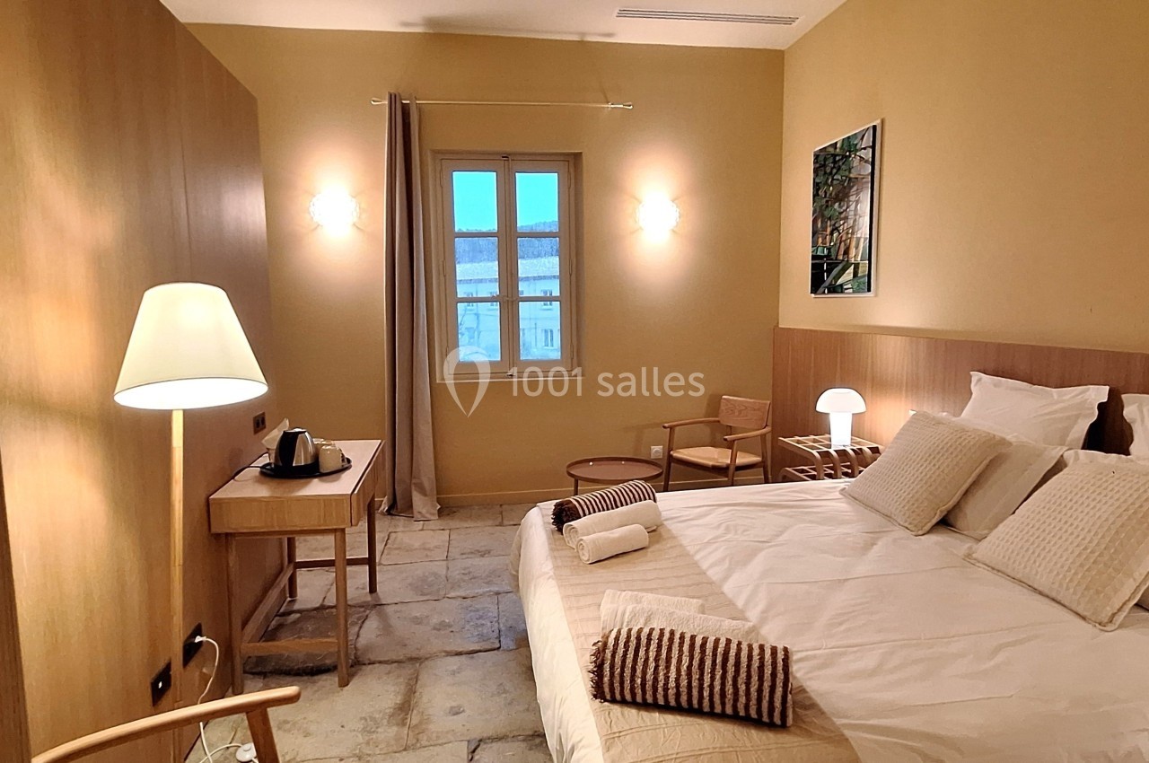 Chambre lumineuse avec lit double, bureau, lampe, deux chaises et fenêtre donnant sur un paysage extérieur.