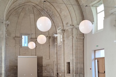 Chambre lumineuse avec lit double, bureau, fauteuils en bois, lampes et fenêtre donnant sur un paysage extérieur.