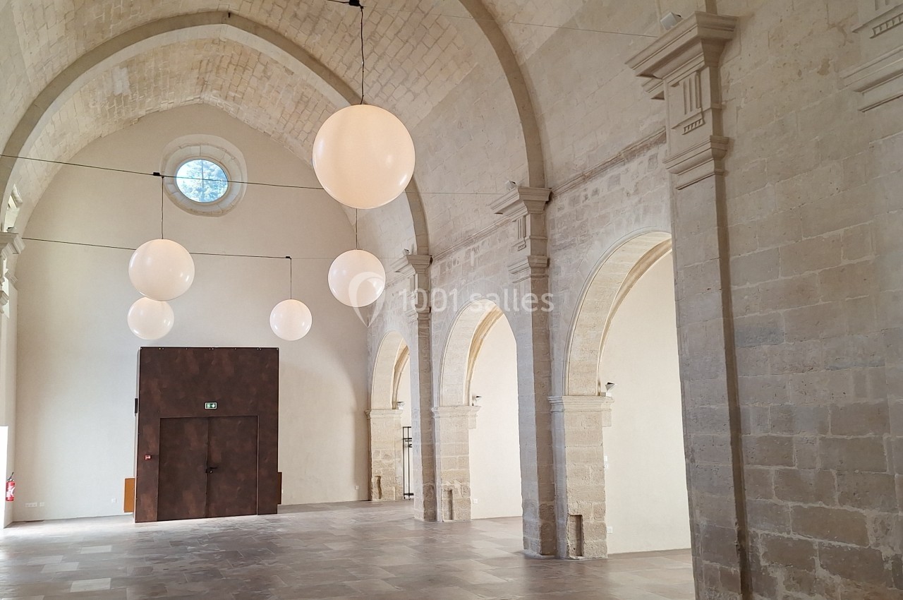 Intérieur d'une salle voûtée en pierre avec des arches, des ballons suspendus et une porte en bois foncé.