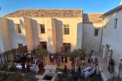 Chambre lumineuse avec lit double, bureau, fauteuils en bois, lampes et fenêtre donnant sur un paysage extérieur.