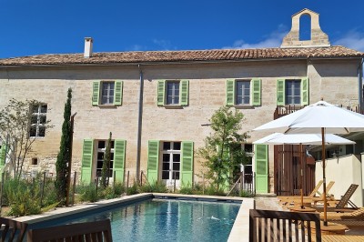 Chambre lumineuse avec lit double, bureau, fauteuils en bois, lampes et fenêtre donnant sur un paysage extérieur.
