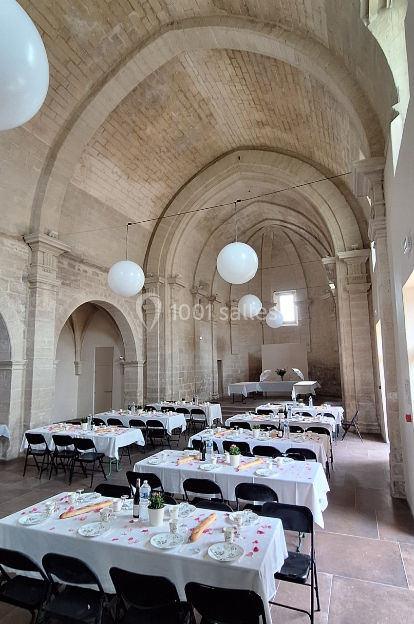 Salle voûtée en pierre aménagée pour un repas, avec tables dressées, nappes blanches et décorations simples.