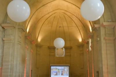 Chambre lumineuse avec lit double, bureau, fauteuils en bois, lampes et fenêtre donnant sur un paysage extérieur.