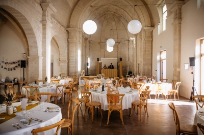 Chambre lumineuse avec lit double, bureau, fauteuils en bois, lampes et fenêtre donnant sur un paysage extérieur.