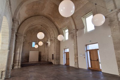 Chambre lumineuse avec lit double, bureau, fauteuils en bois, lampes et fenêtre donnant sur un paysage extérieur.