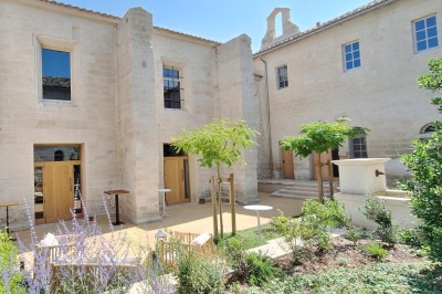 Chambre lumineuse avec lit double, bureau, fauteuils en bois, lampes et fenêtre donnant sur un paysage extérieur.