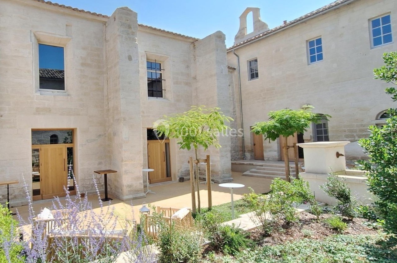 Cour intérieure d'un bâtiment en pierre claire avec végétation, tables et chaises disposées sur une terrasse.
