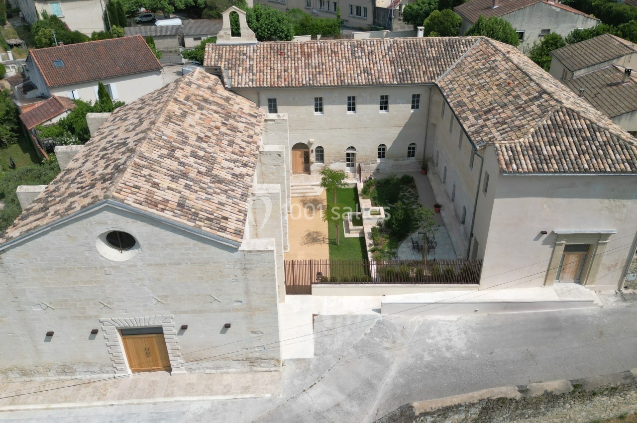 Vue aérienne d'un bâtiment en pierre avec toits en tuiles, entouré de maisons et d'espaces verts.