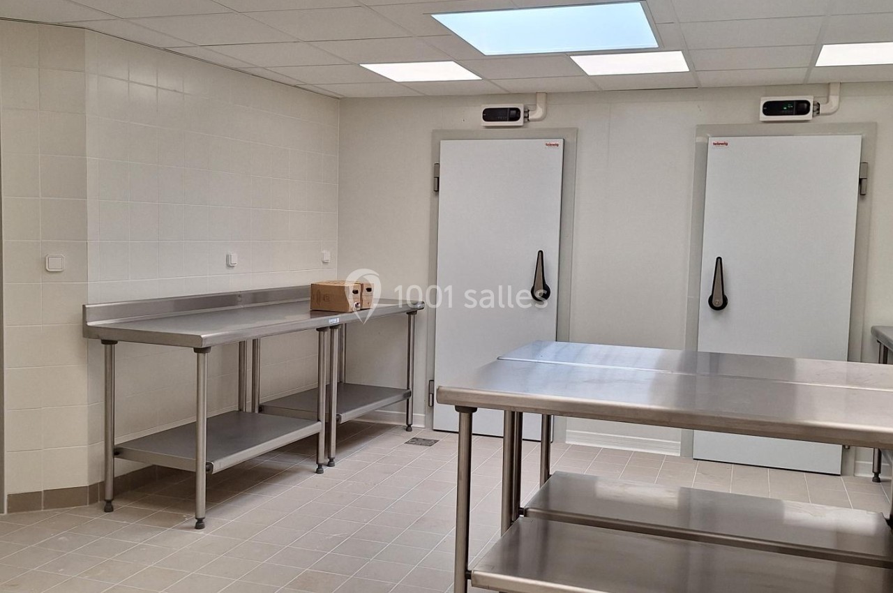 Cuisine professionnelle avec plans de travail en inox, deux grandes chambres froides et éclairage au plafond.