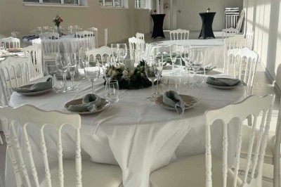 Jardin aménagé avec pelouse, terrasse en pavés, tables hautes et pergola, entouré de bâtiments en briques.