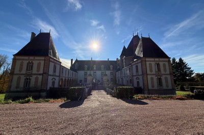 Château en briques rouges entouré de pelouses et d'arbres, sous un ciel clair et ensoleillé.