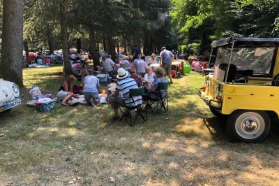 Château en briques rouges entouré de pelouses et d'arbres, sous un ciel clair et ensoleillé.