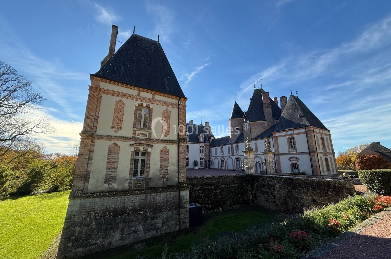 Château historique en pierre et briques, entouré de verdure, sous un ciel bleu dégagé.